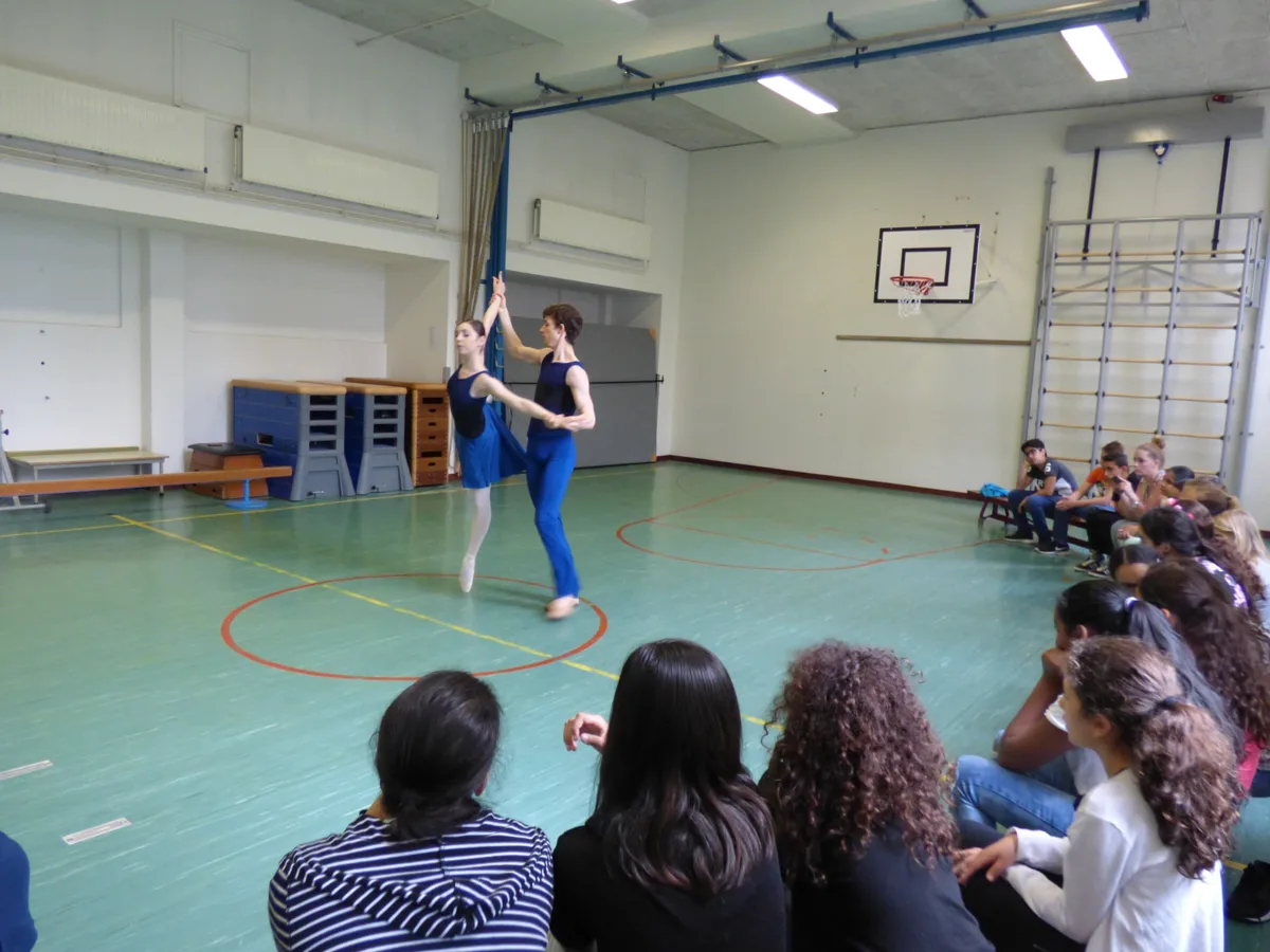 Twee dansers van de Junior Company dansen voor leerlingen in een gymzaal