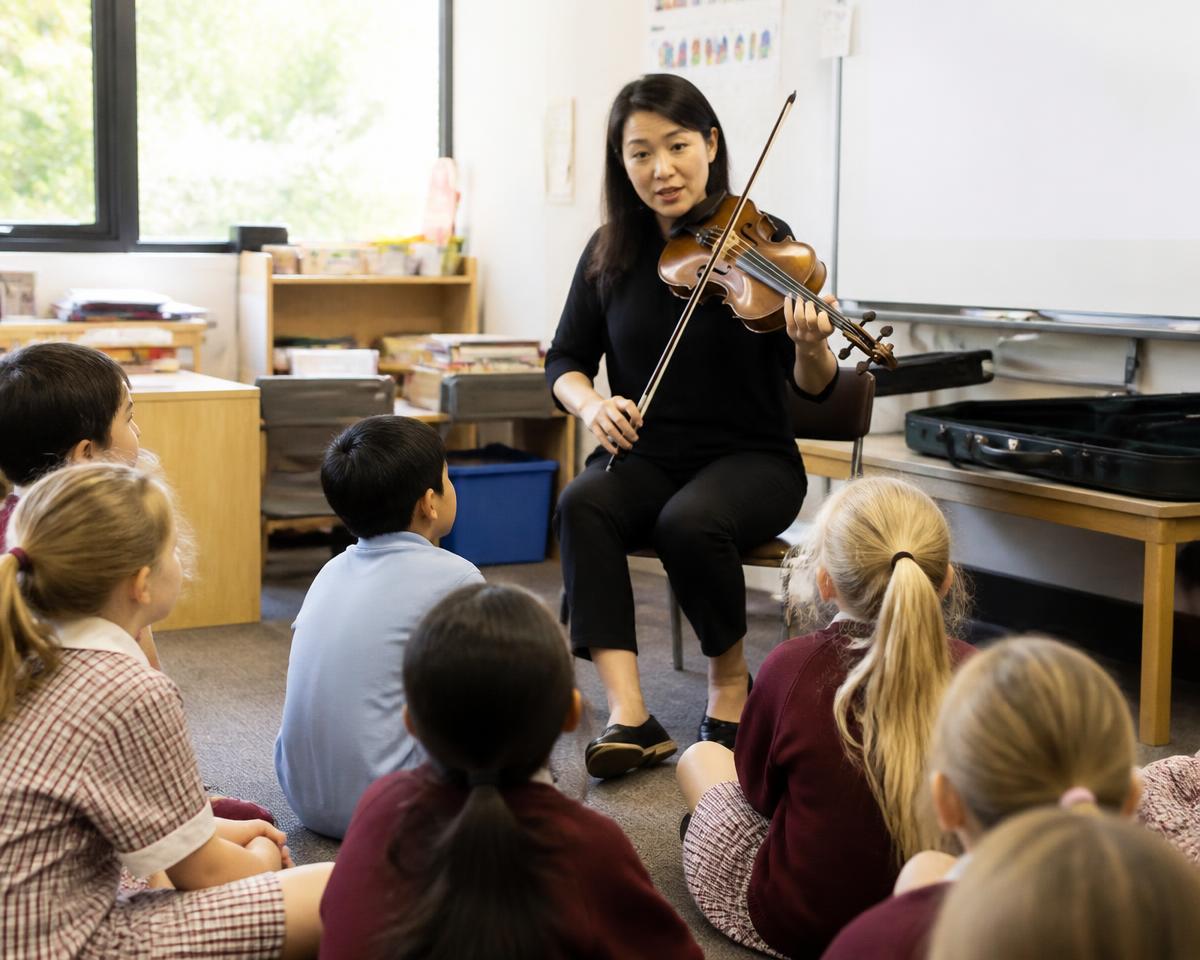 Jonge musicus geeft een masterclass viool aan een groep schoolkinderen in de klas