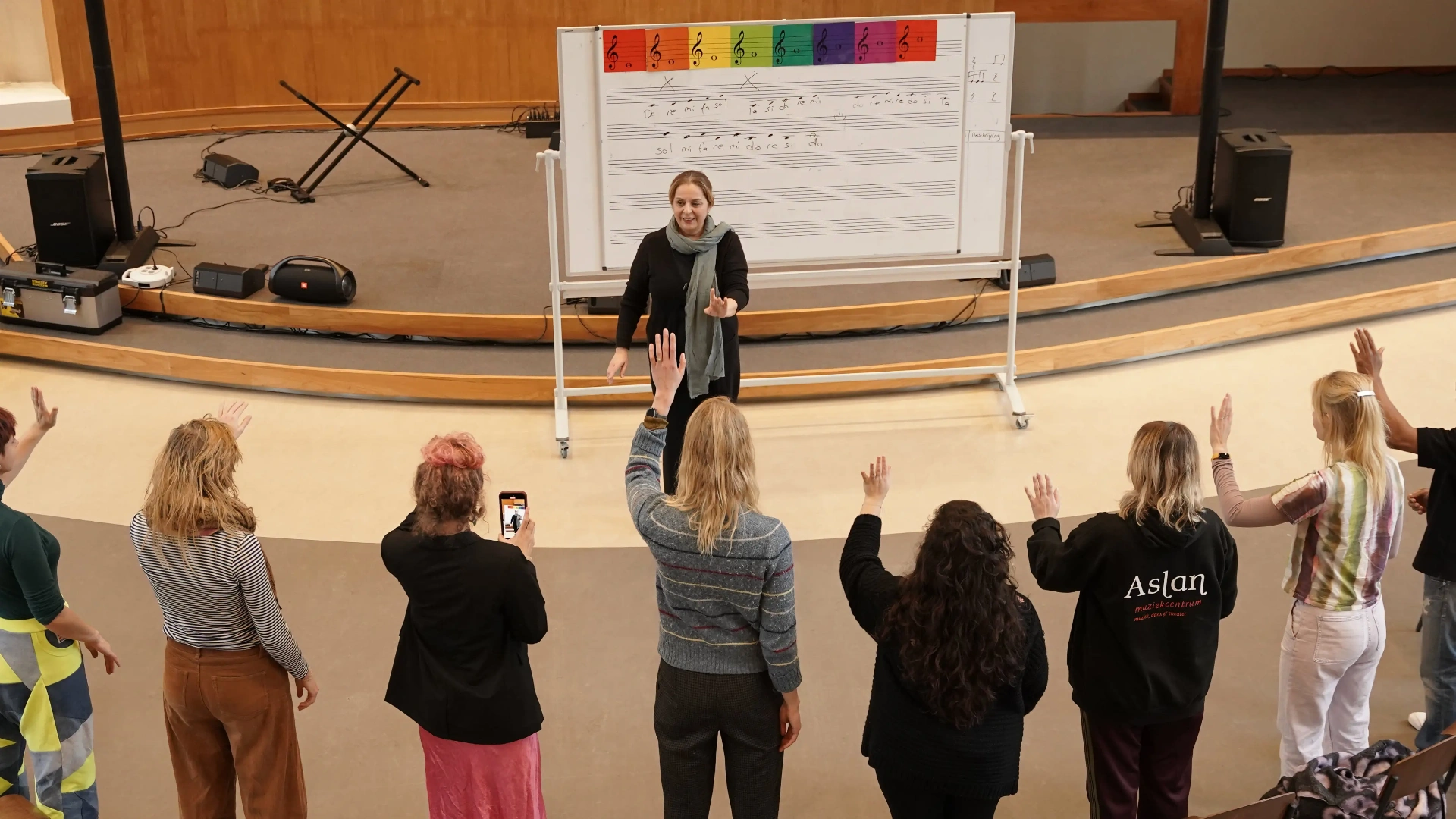 Docent geeft solfège-les met handgebaren aan een groep deelnemers
