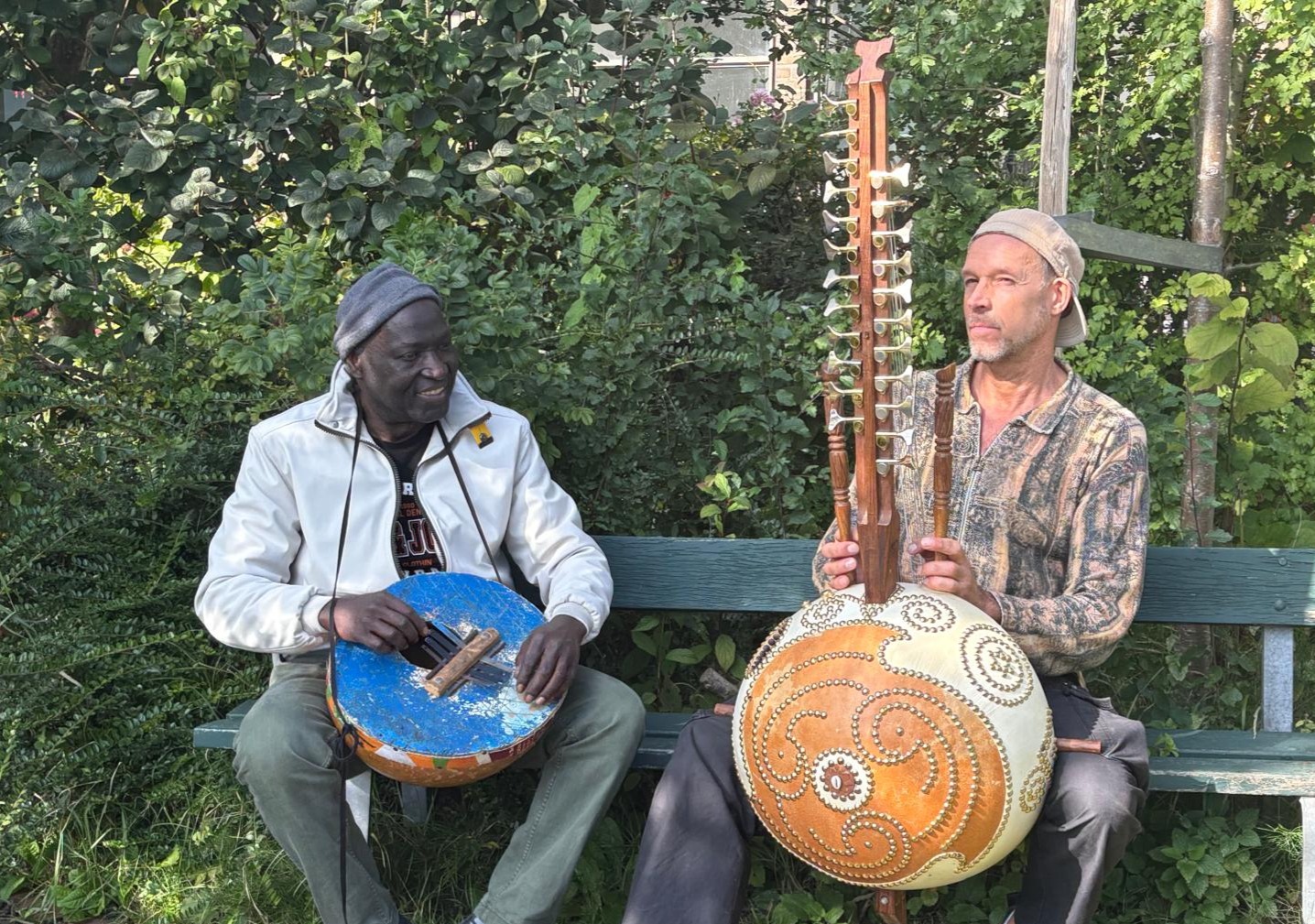 Twee musici van Casa di Mansa met kora en percussie in een groene tuin